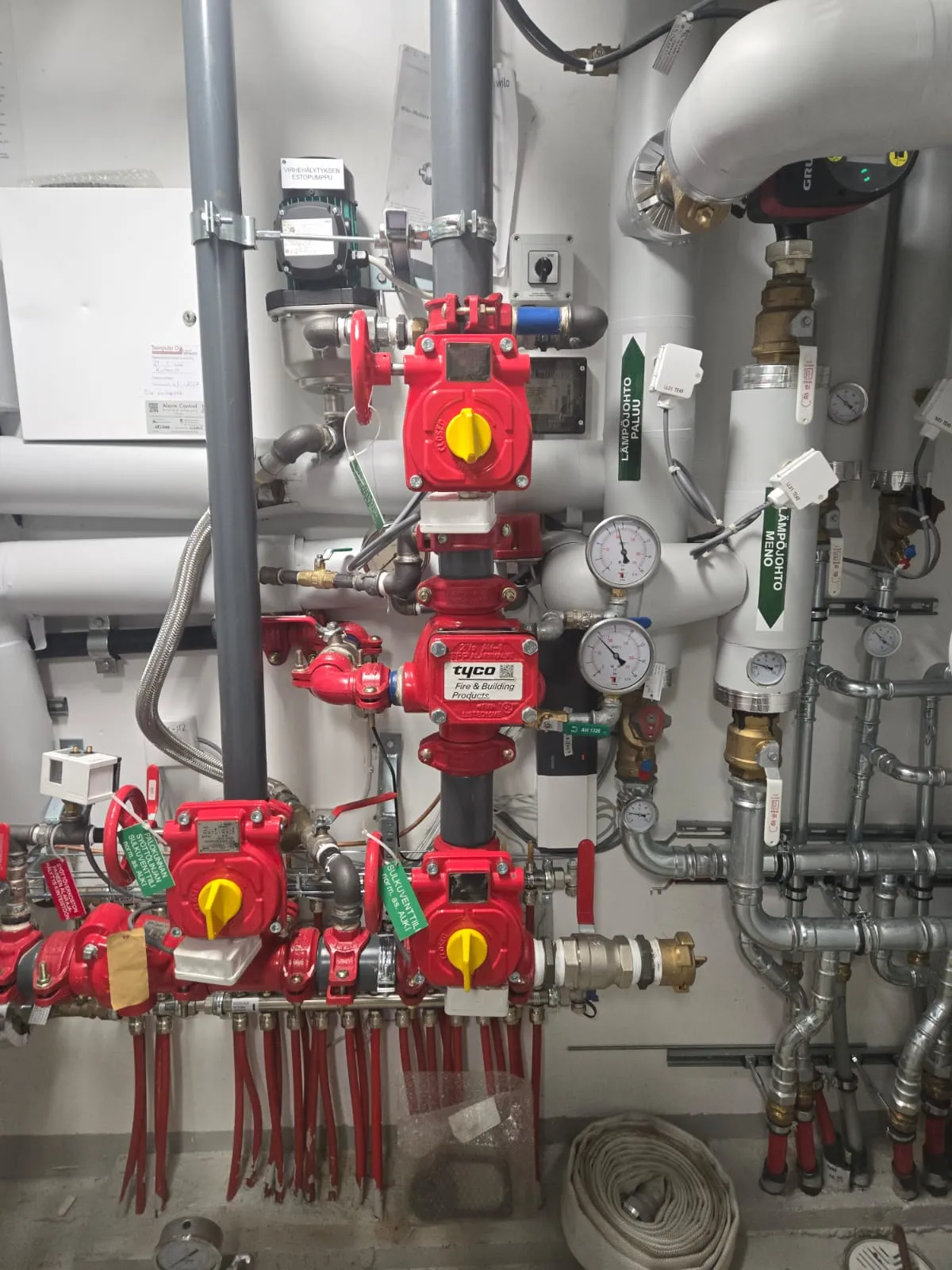 Monimutkainen putkisto, jossa on punaisia venttiilejä, painemittareita ja valkoisia putkia, sekä tekstiä suomeksi.